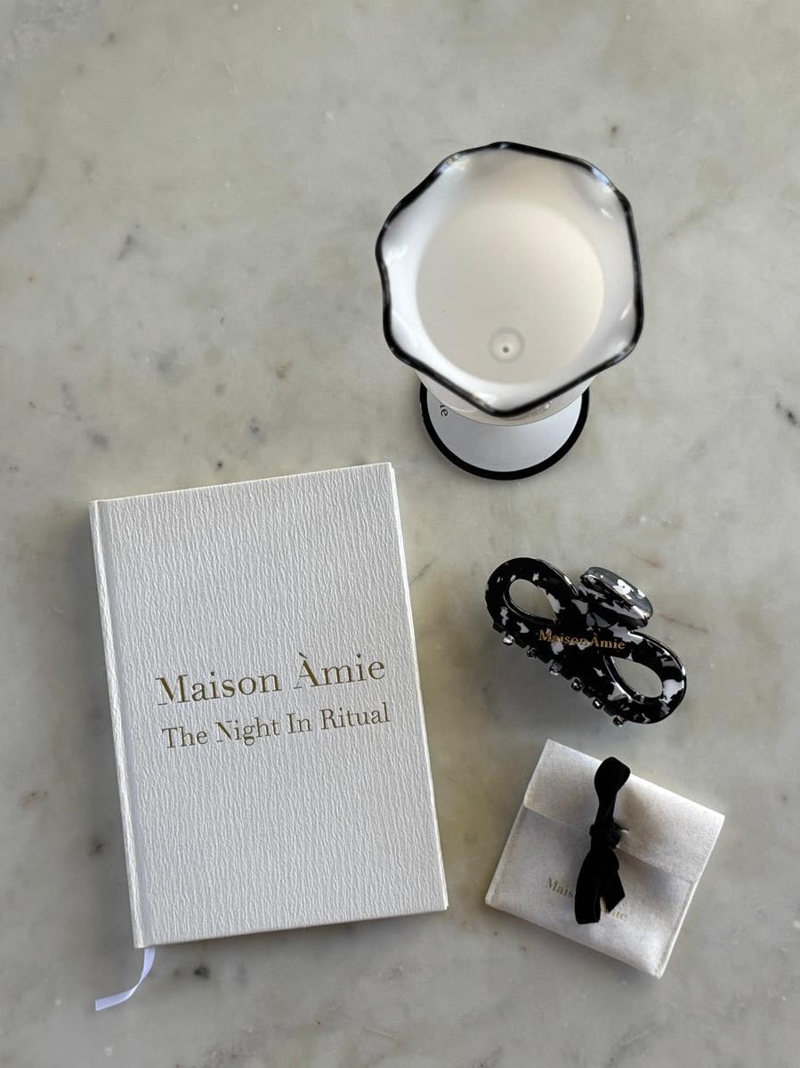 Maison Àmie Night-In Ritual flatlay - the journal, a bracelet pouch, infinity hair clip and Fill-Me-In glass on marble. 